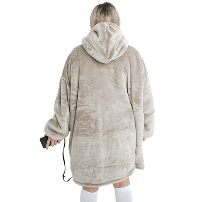 Eine Person, die den Flauschiger Beige Hoti von The Hoti trägt, einen übergroßen Plüschhoodie mit Kapuze, steht mit dem Rücken zur Kamera. Sie hält ein Telefon in einer Hand und trägt kniehohe weiße Socken.
