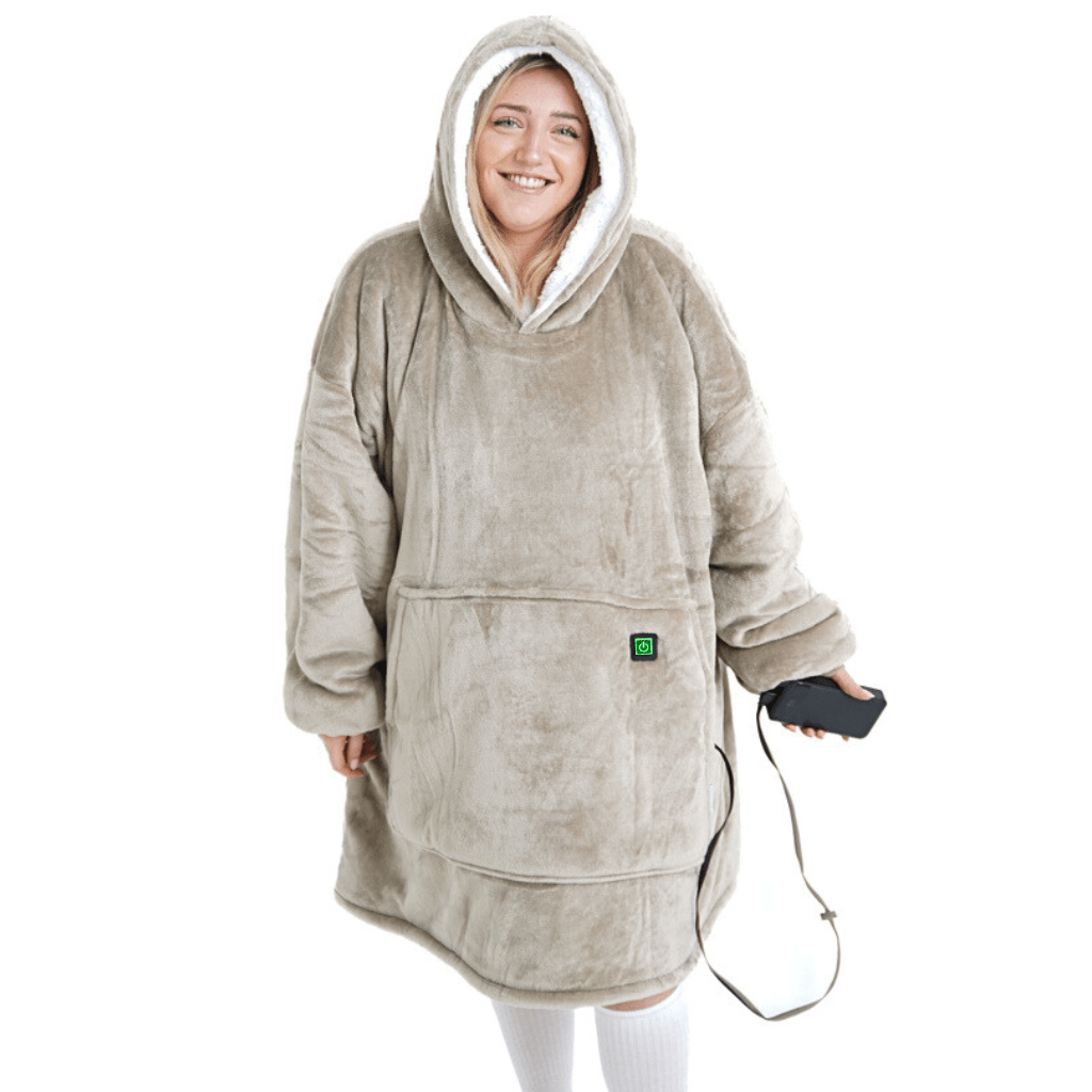 Eine Person trägt einen großen, gemütlichen Flauschiger Beige Hoti von The Hoti mit flauschiger Textur und Vordertasche und lächelt, während sie ein schwarzes Smartphone hält. Die Kapuzendecke bedeckt die Person vollständig und ähnelt einem übergroßen Pullover.