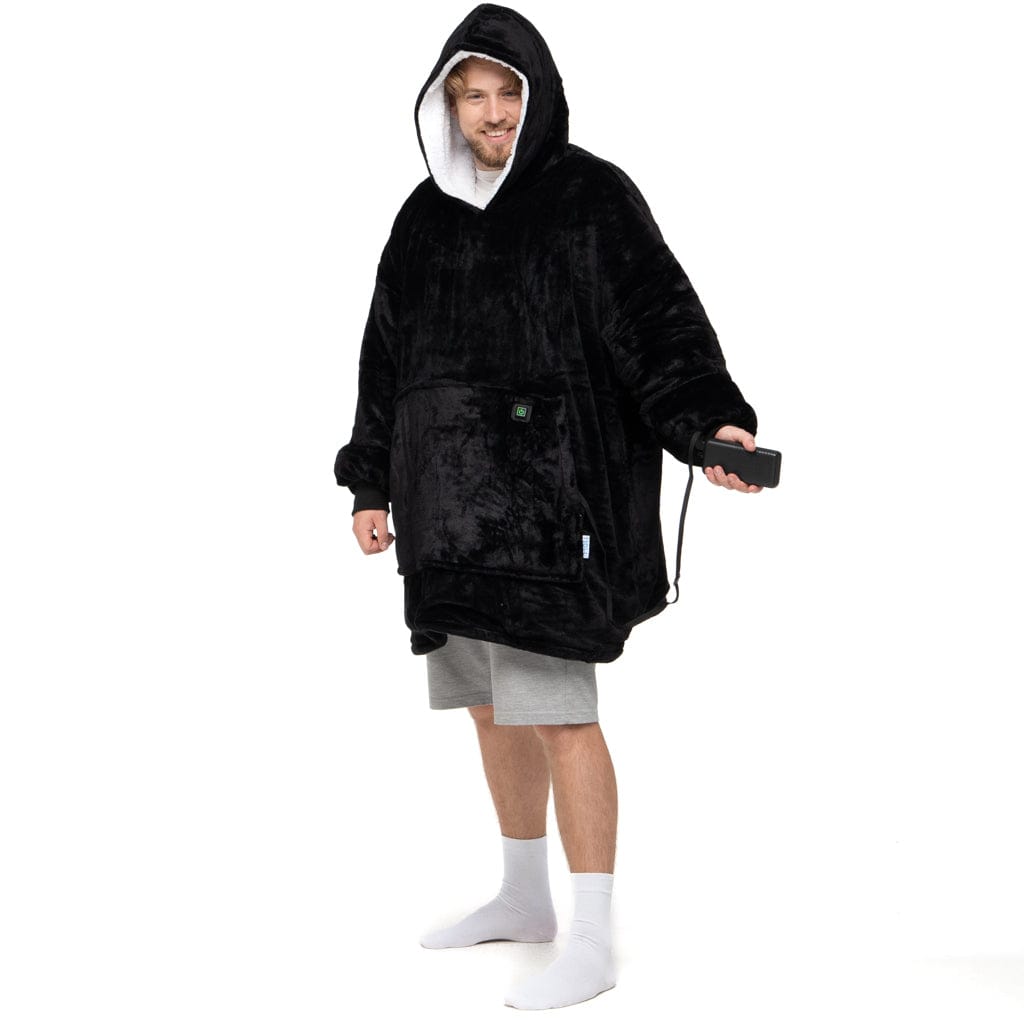 Eine Person trägt „Schwarzes Wunder Hoti“, ein großes, schwarzes, flauschiges Kapuzensweatshirt mit einer Vordertasche der Marke The Hoti und graue Shorts und hält ein Smartphone. Mit hochgezogener Kapuze steht sie vor einem schlichten weißen Hintergrund.