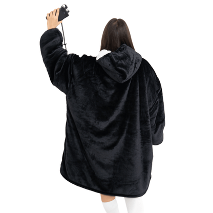 Eine Person, die ein Schwarzes Wunder Hoti von The Hoti trägt, steht mit dem Rücken zur Kamera und hält in der erhobenen Hand eine Tasse mit Riemen. Sie trägt kniehohe weiße Socken vor einem schlichten weißen Hintergrund.