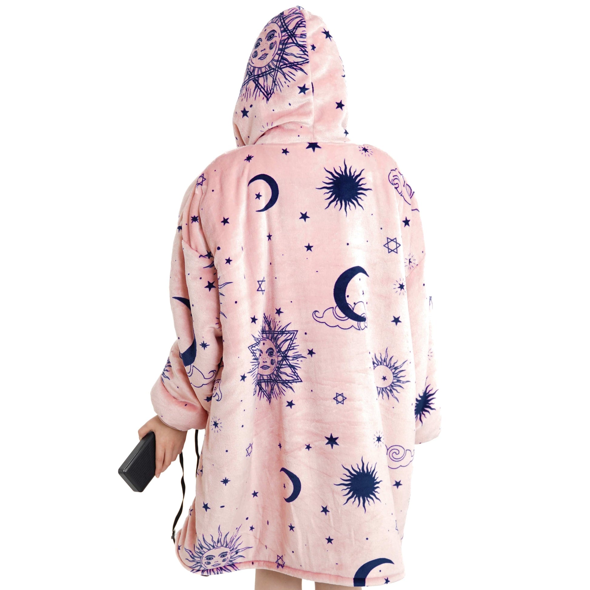 Eine Person trägt den Träumender Stern Hoti, einen übergroßen rosa Kapuzenpullover von The Hoti, der mit einem himmlischen Design aus Sonnen, Monden, Sternen und Wolken verziert ist. Die Kapuze ist hochgezogen und die Person hält einen schwarzen Gegenstand – möglicherweise eine kleine Tasche oder ein Telefon – in der linken Hand.